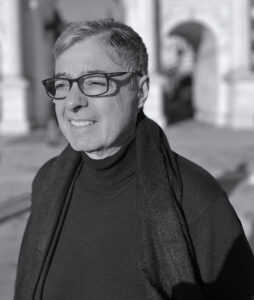 A black and white photograph of a man wearing glasses, black shirt and scarf. He is against the sun, so his face is a little frowned.